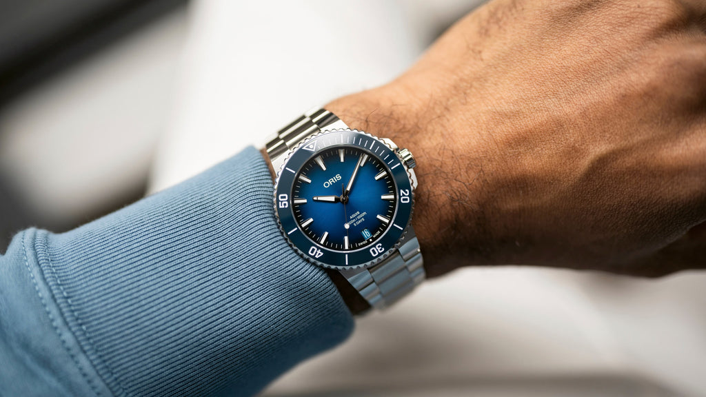 Oris Aquis watch with a striking blue dial, stainless steel case, and a unidirectional rotating bezel, showcasing its sleek design and robust functionality. On male model view.