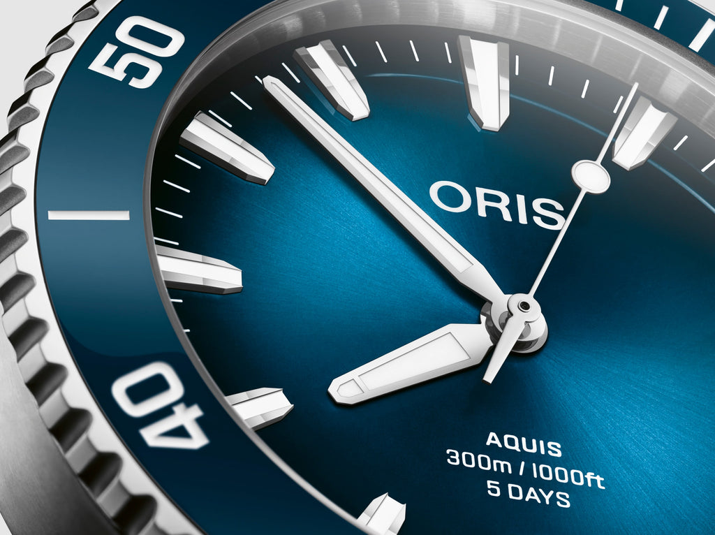 Oris Aquis watch with a striking blue dial, stainless steel case, and a unidirectional rotating bezel, showcasing its sleek design and robust functionality. Close up of dial view.