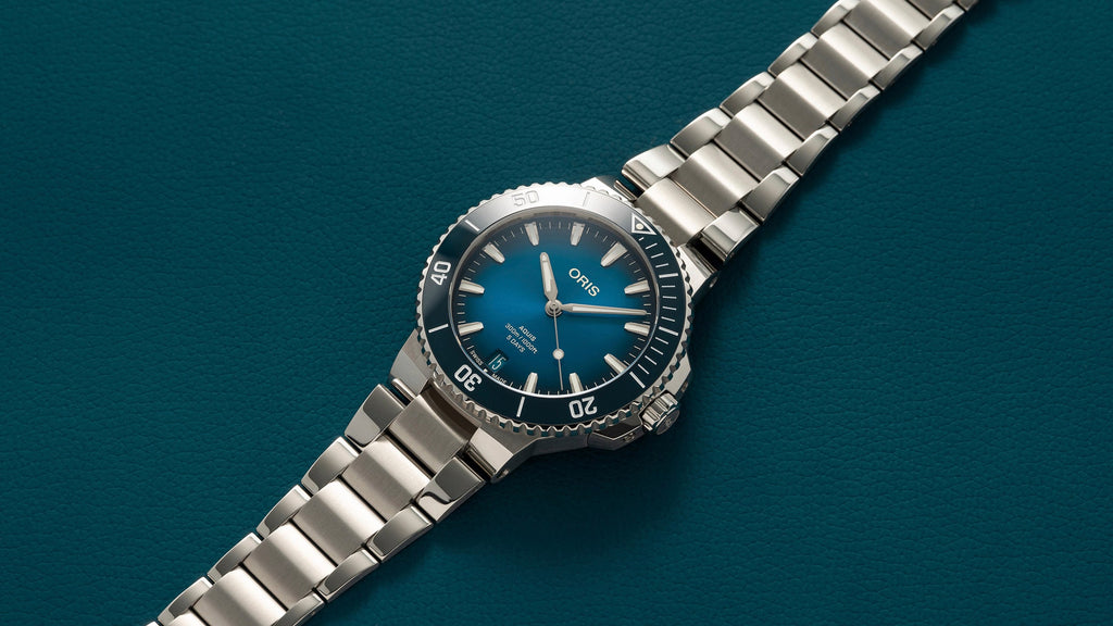 Oris Aquis watch with a striking blue dial, stainless steel case, and a unidirectional rotating bezel, showcasing its sleek design and robust functionality. Full laid out view.