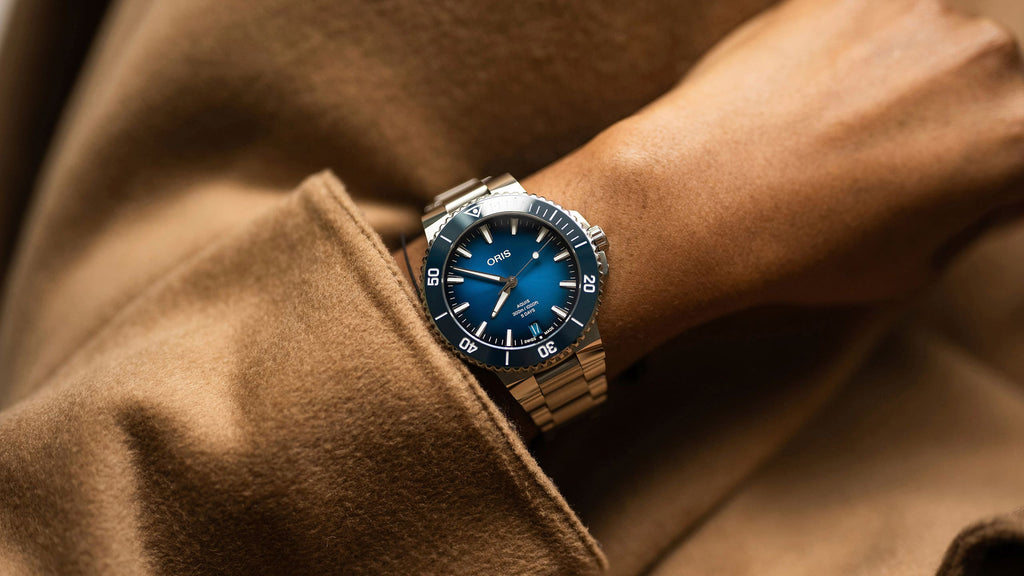 Oris Aquis watch with a striking blue dial, stainless steel case, and a unidirectional rotating bezel, showcasing its sleek design and robust functionality. View on female model.