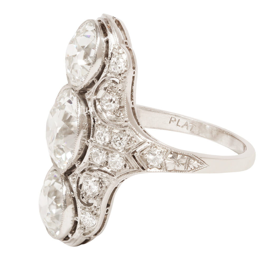 Elegant Edwardian three diamond dinner ring. Diamonds are bezel-set vertically. Small diamonds cover the pierced surface of the ring. Side view.