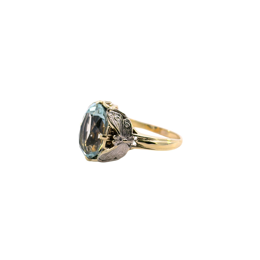 Profile view of a two-tone gold aquamarine ring showing the open-sided setting, butterfly shoulders and yellow gold band.