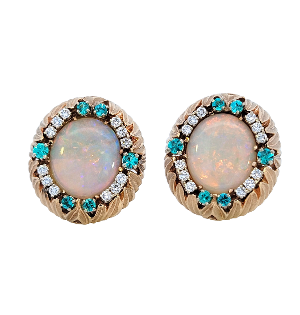 Pair of oval-shaped white opal earrings framed by diamonds and alternating Paraiba Tourmalines in a rounded carved leaf gold frame.