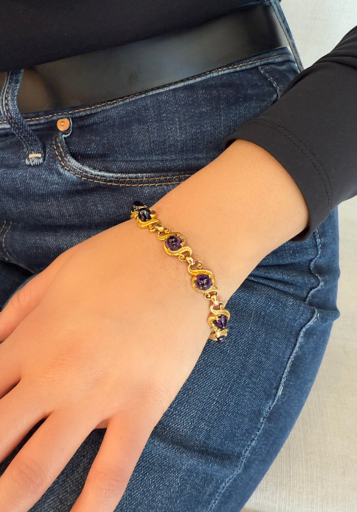 Arts and Crafts bracelet with bullet-shaped Amethyst cabochons set into  individual hand-made gold swirls shown on model's hand wearing jeans and a black belt. 