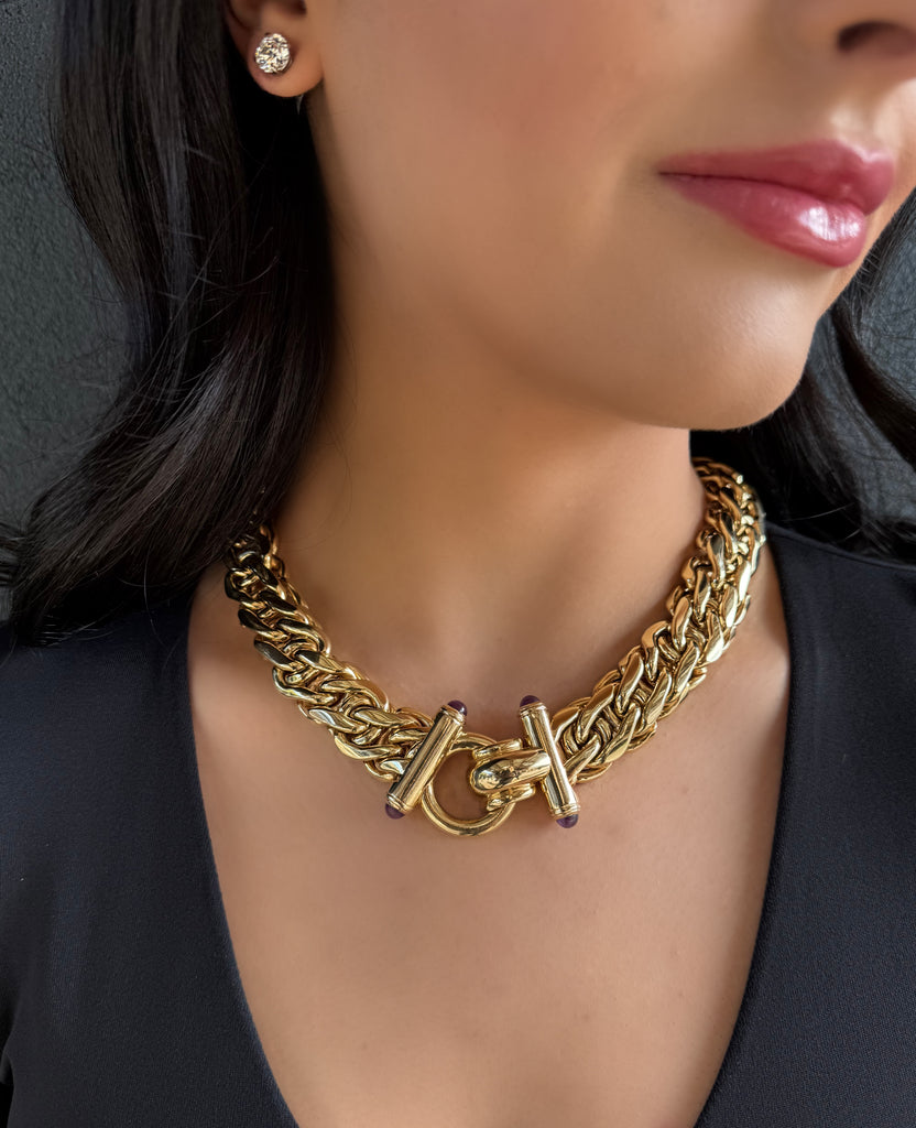 Wide braided yellow gold collar necklace with hinged loop clasp that is finished by amethyst cabochon studded finials. On model.