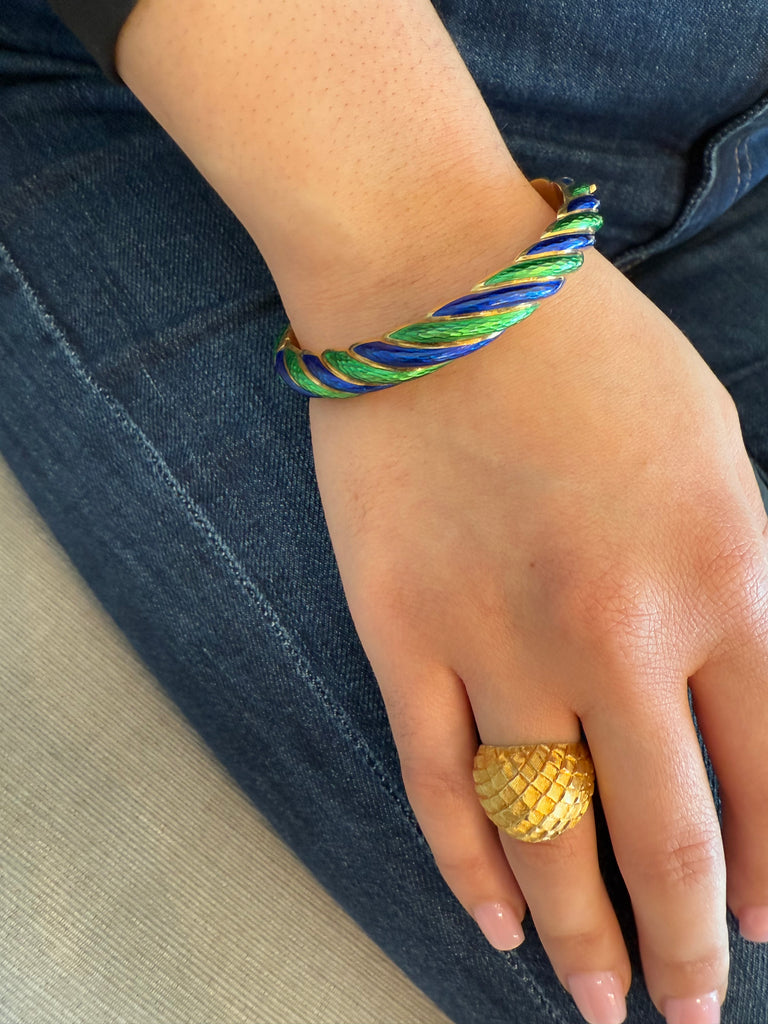Cartier Guilloche blue and green enameled bangle gold bracelet with concealed clasp and safety chain. Worn on model with domed gold textured ring and denim.