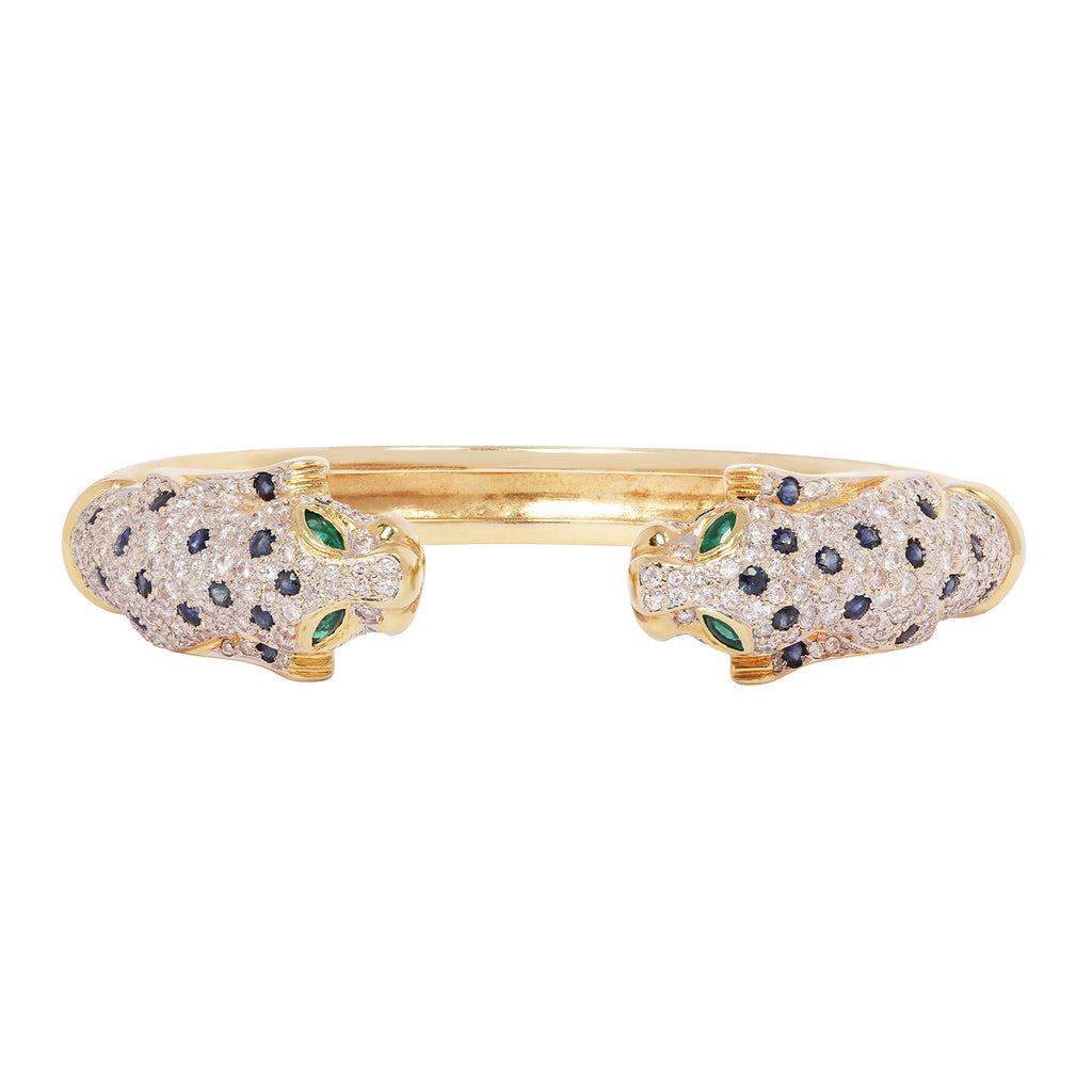 Front view of a luxury 18K yellow gold cuff bracelet with pavé diamond leopard heads, sapphire accents, and emerald eyes.