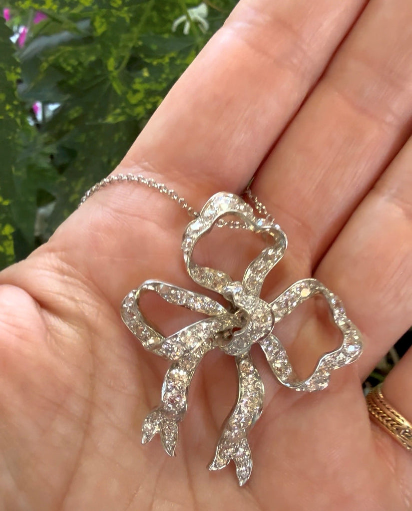 Vintage Edwardian platinum and diamond bow pendant shown on model for scale and neckline appearance.
