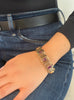 Openwork gold square link bracelet with 10 oval bezel-set magenta sapphires shown on model wearing jeans and a black shirt.