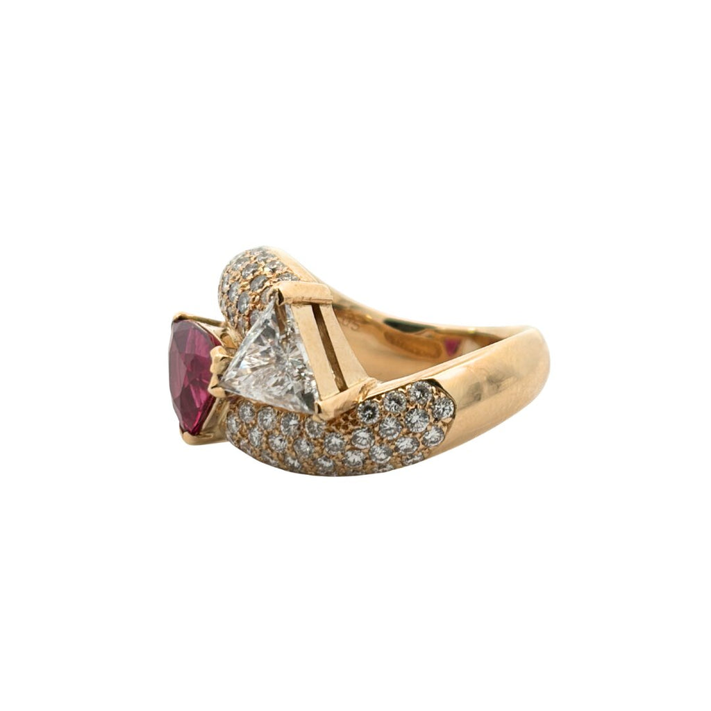 Side view of a gold bypass ring highlighting the raised trillion-cut diamond setting beside the ruby and pavé diamond accents.