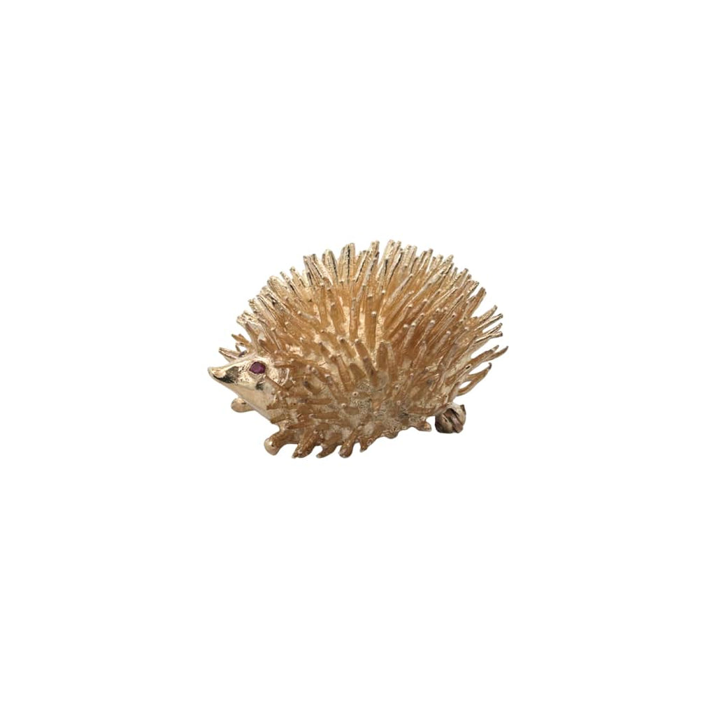Three-quarter view of a vintage gold hedgehog brooch highlighting ruby eyes and detailed quill texture.