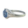 Edwardian-inspired platinum ring with a 6.16ct round blue sapphire and 54 diamond accents, detailed with milgrain and engraving.